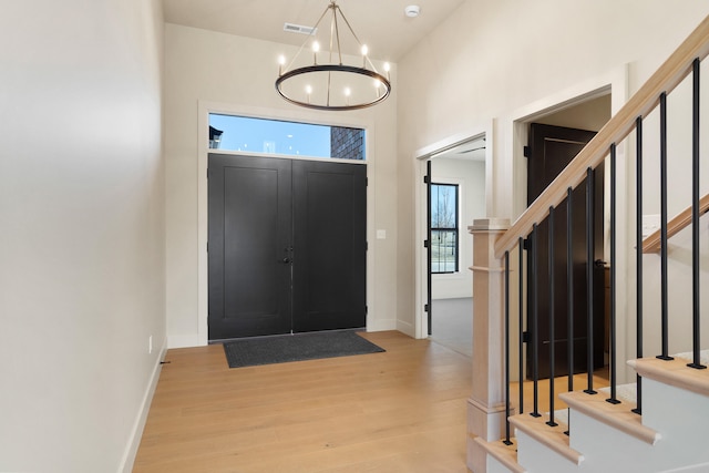 entryway featuring stairs, an inviting chandelier, light wood-style flooring, and baseboards