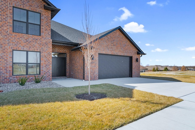 traditional-style house with brick siding, a shingled roof, concrete driveway, a front yard, and a garage