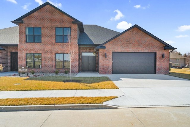 traditional-style house with roof with shingles, an attached garage, a front lawn, concrete driveway, and brick siding