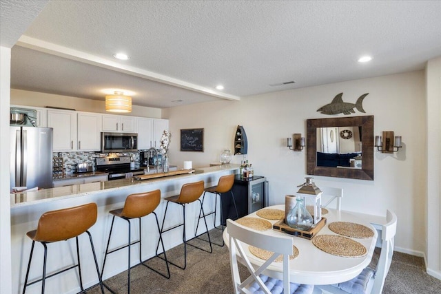 kitchen with stainless steel appliances, white cabinetry, dark colored carpet, and kitchen peninsula