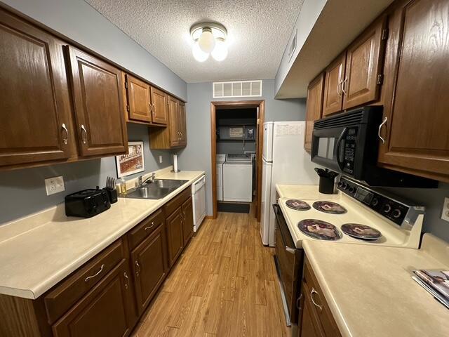 kitchen featuring light countertops, light wood-style floors, a sink, white appliances, and independent washer and dryer