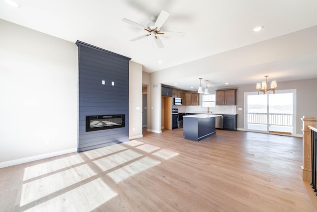 unfurnished living room featuring a large fireplace, ceiling fan with notable chandelier, and light wood-type flooring