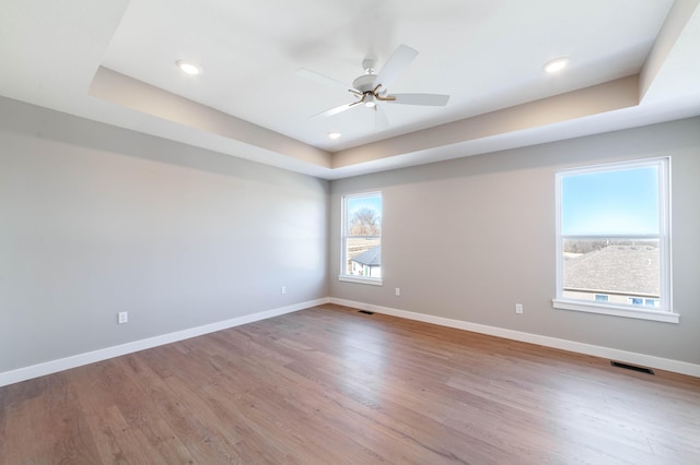 empty room with a tray ceiling, light hardwood / wood-style floors, and ceiling fan