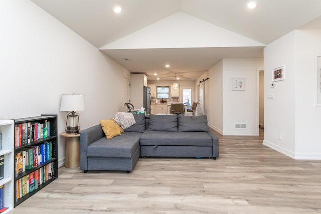 living room with a barn door, lofted ceiling, and light hardwood / wood-style flooring