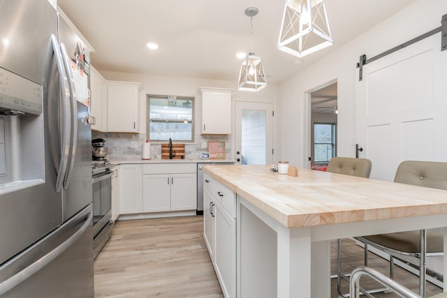 kitchen with a kitchen bar, wooden counters, appliances with stainless steel finishes, a barn door, and white cabinets