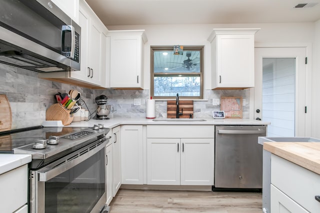 kitchen with sink, white cabinetry, stainless steel appliances, light hardwood / wood-style floors, and decorative backsplash