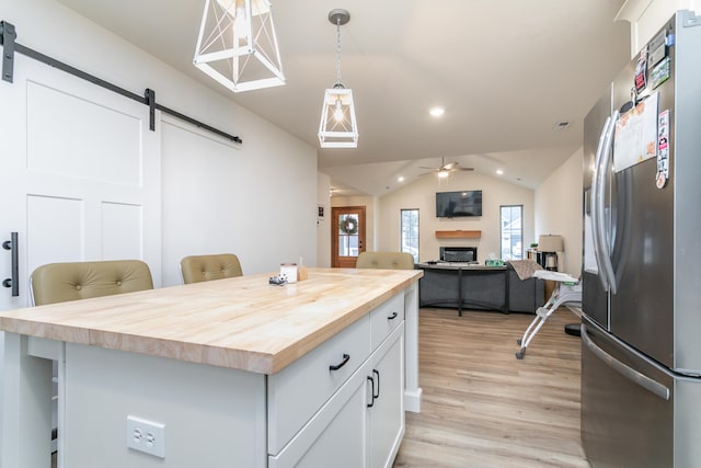 kitchen with stainless steel refrigerator with ice dispenser, a barn door, a breakfast bar, and white cabinets