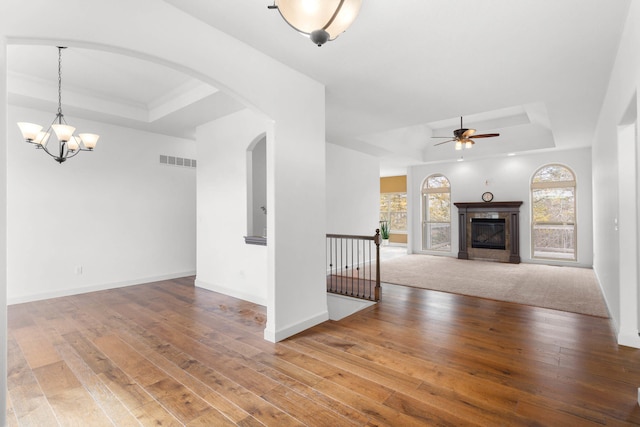 unfurnished living room featuring ceiling fan with notable chandelier, a raised ceiling, and hardwood / wood-style floors