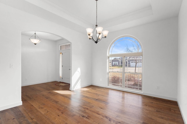 empty room featuring ornamental molding, an inviting chandelier, dark hardwood / wood-style flooring, and a tray ceiling