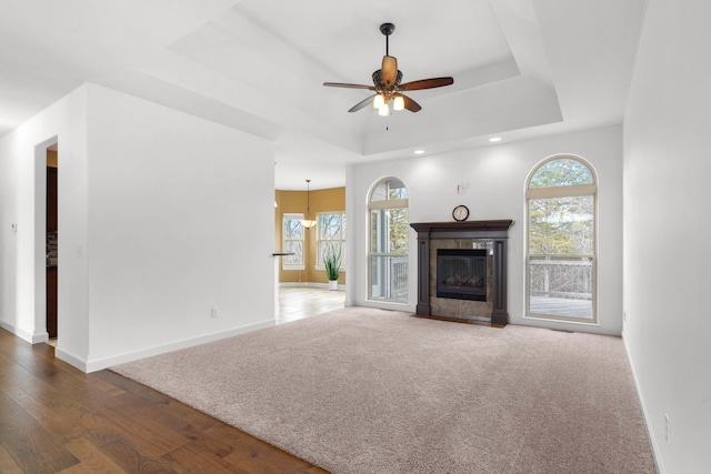 unfurnished living room featuring a tiled fireplace, ceiling fan, dark hardwood / wood-style flooring, and a raised ceiling