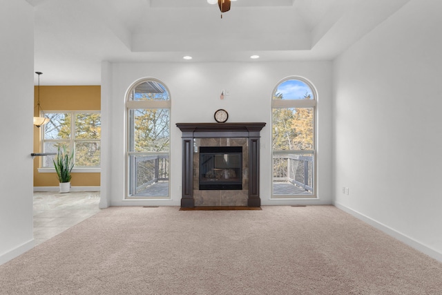 unfurnished living room with a tiled fireplace, light colored carpet, and a raised ceiling