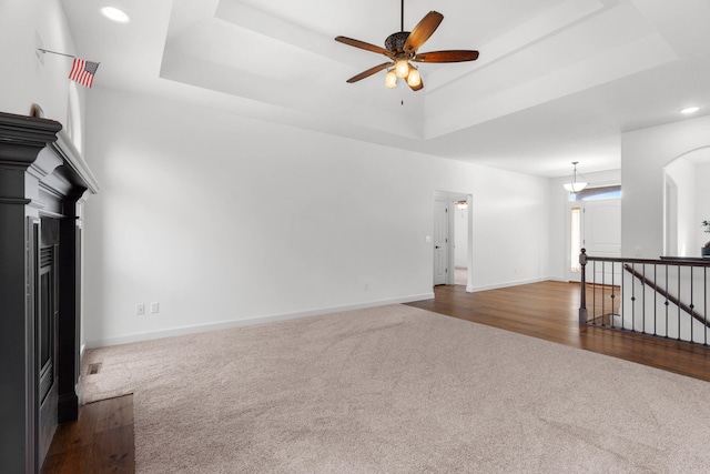 unfurnished living room with a raised ceiling, dark colored carpet, and ceiling fan