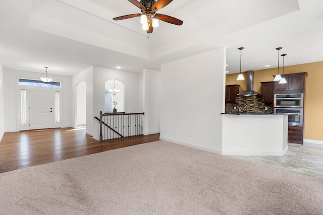 unfurnished living room featuring sink, ceiling fan with notable chandelier, carpet floors, and a raised ceiling