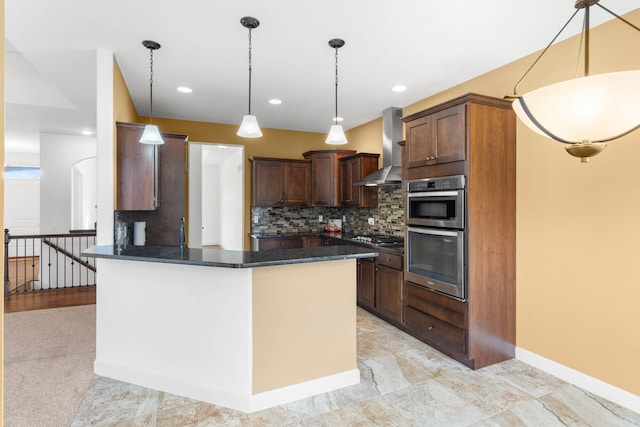 kitchen featuring appliances with stainless steel finishes, pendant lighting, tasteful backsplash, dark stone counters, and wall chimney range hood