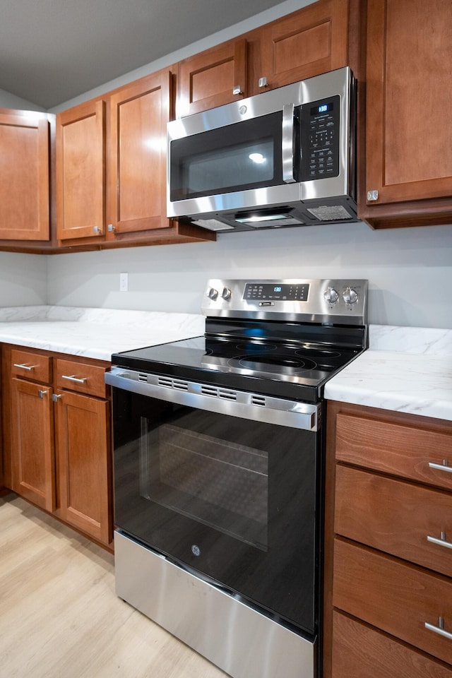 kitchen with light stone counters, appliances with stainless steel finishes, and light hardwood / wood-style floors