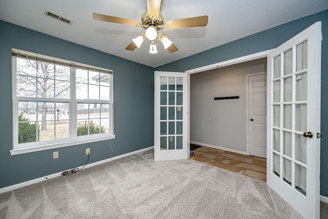 carpeted spare room featuring ceiling fan, french doors, and a textured ceiling