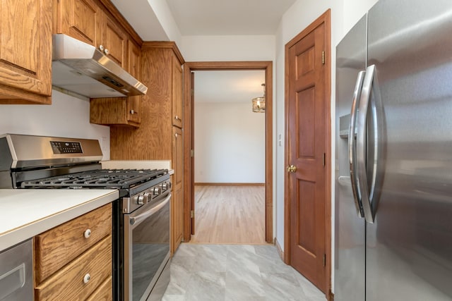 kitchen featuring brown cabinetry, baseboards, light countertops, under cabinet range hood, and appliances with stainless steel finishes