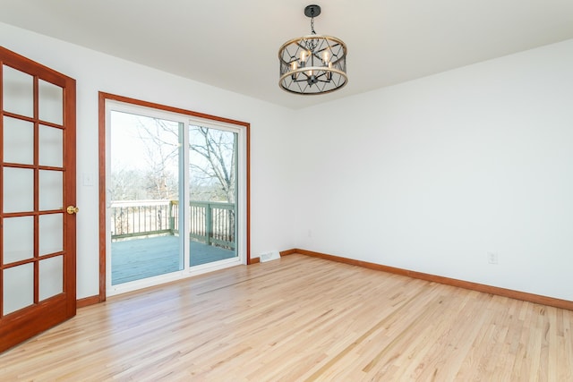 empty room featuring light wood-style flooring, a notable chandelier, visible vents, and baseboards