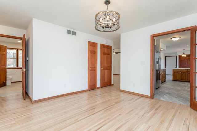 unfurnished bedroom featuring visible vents, baseboards, light wood-type flooring, and stainless steel refrigerator with ice dispenser