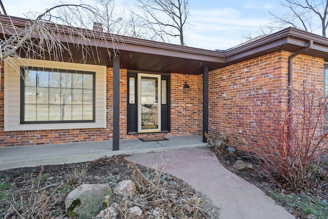 view of exterior entry featuring a porch and brick siding