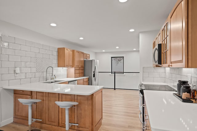 kitchen with light wood finished floors, a breakfast bar area, a peninsula, stainless steel appliances, and a sink