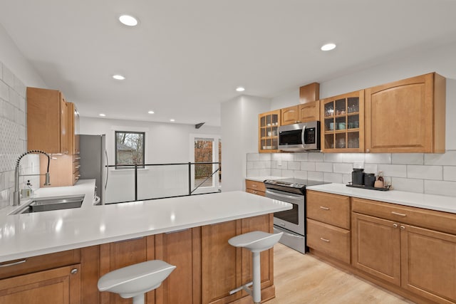 kitchen with a peninsula, a sink, light countertops, appliances with stainless steel finishes, and a kitchen bar