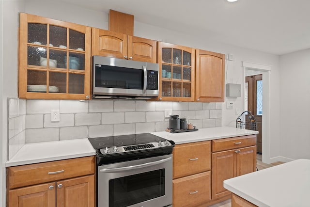 kitchen with tasteful backsplash, light countertops, appliances with stainless steel finishes, glass insert cabinets, and baseboards