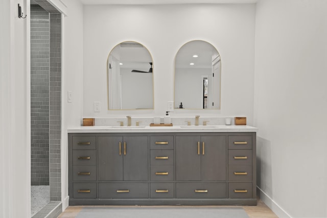 full bath featuring double vanity, baseboards, a tile shower, and a sink