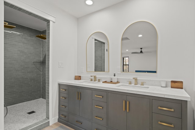 full bath featuring double vanity, ceiling fan, a tile shower, and a sink