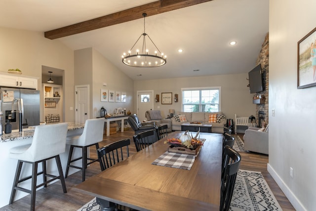 dining room with dark wood-type flooring, high vaulted ceiling, a notable chandelier, a stone fireplace, and beamed ceiling