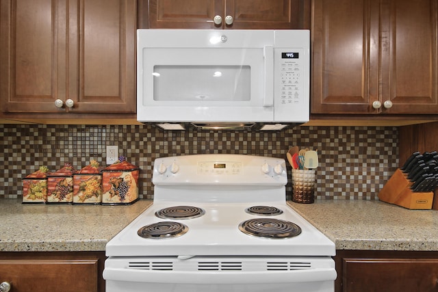 kitchen featuring white appliances, light stone counters, and backsplash