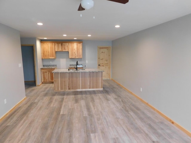 kitchen featuring sink, a kitchen island with sink, light stone counters, light brown cabinets, and light wood-type flooring