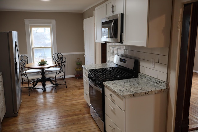 kitchen with appliances with stainless steel finishes, tasteful backsplash, white cabinetry, light stone countertops, and light hardwood / wood-style flooring