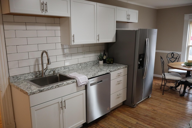 kitchen featuring sink, white cabinetry, appliances with stainless steel finishes, hardwood / wood-style floors, and decorative backsplash