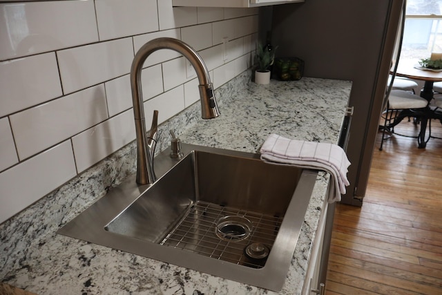 room details featuring sink, decorative backsplash, white cabinets, and hardwood / wood-style flooring