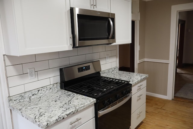 kitchen featuring light hardwood / wood-style flooring, light stone countertops, gas stove, white cabinets, and decorative backsplash