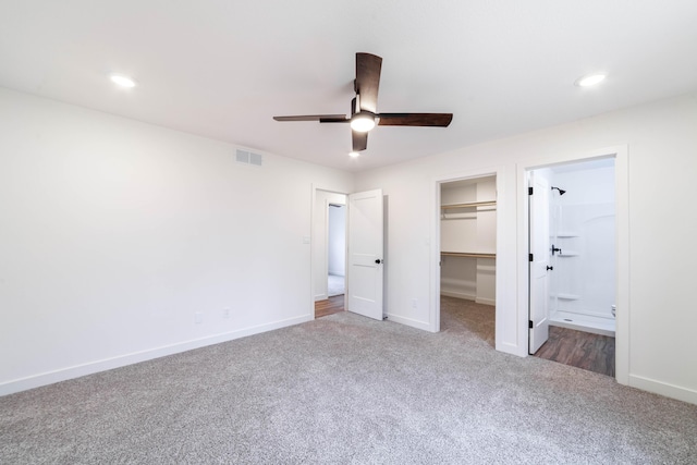 unfurnished bedroom featuring ceiling fan, ensuite bathroom, carpet, a walk in closet, and a closet