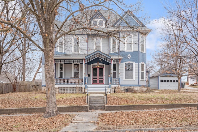 victorian-style house featuring a garage, a porch, and an outbuilding