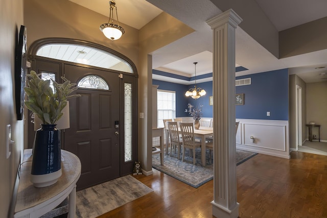 foyer entrance featuring decorative columns, a raised ceiling, dark hardwood / wood-style floors, and an inviting chandelier