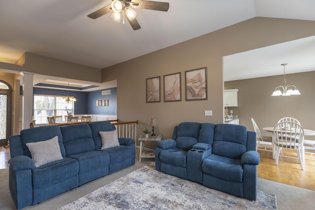 living room with lofted ceiling, a tray ceiling, ceiling fan with notable chandelier, and decorative columns