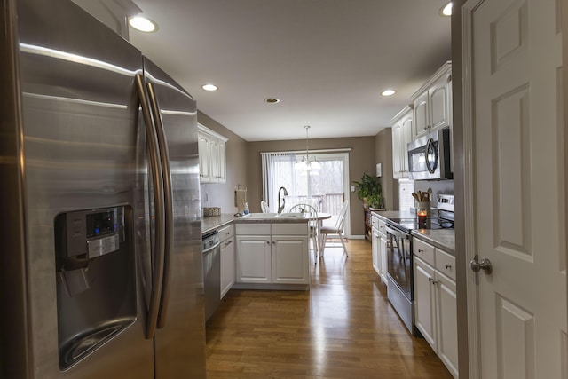 kitchen with decorative light fixtures, white cabinets, kitchen peninsula, stainless steel appliances, and dark wood-type flooring