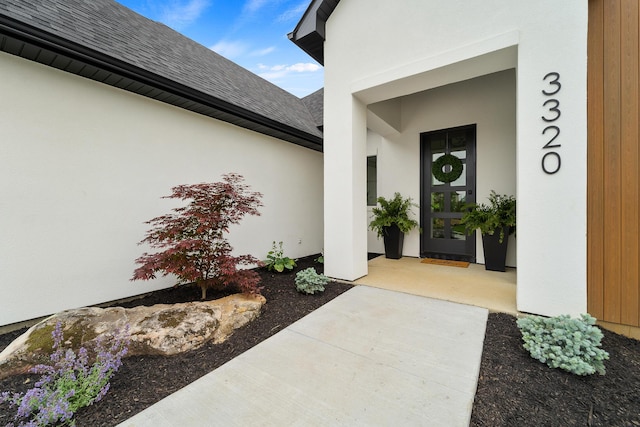 doorway to property featuring stucco siding and roof with shingles