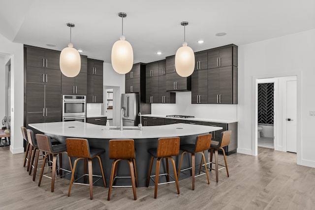 kitchen featuring dark brown cabinetry, light countertops, a large island with sink, and decorative light fixtures