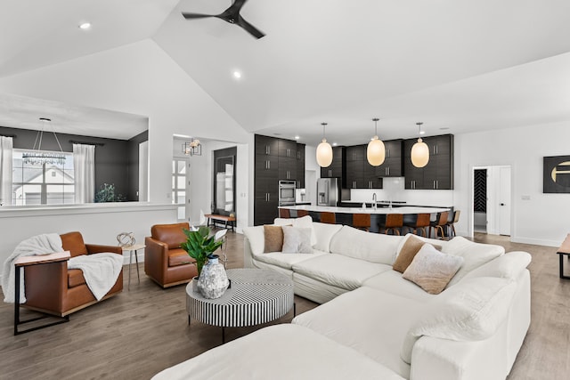 living area with light wood finished floors, recessed lighting, high vaulted ceiling, baseboards, and ceiling fan with notable chandelier