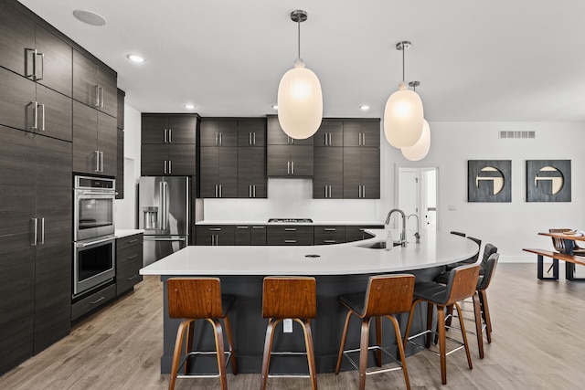 kitchen with appliances with stainless steel finishes, pendant lighting, a kitchen island with sink, and a sink