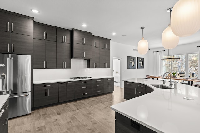 kitchen featuring light countertops, hanging light fixtures, appliances with stainless steel finishes, light wood-style floors, and a sink