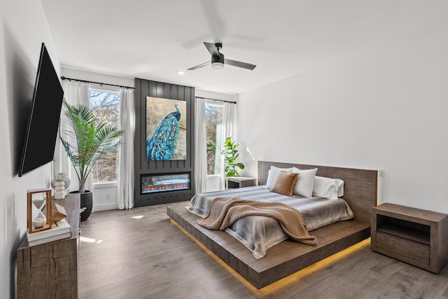 bedroom featuring ceiling fan, a fireplace, and wood finished floors