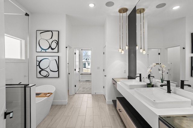 bathroom with a freestanding tub, recessed lighting, a sink, wood finished floors, and double vanity