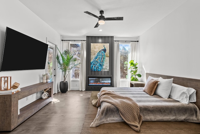 bedroom featuring a ceiling fan, a large fireplace, and wood finished floors