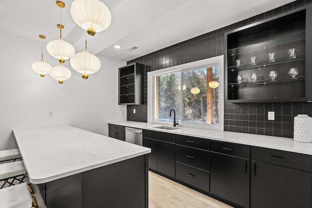 kitchen with backsplash, dark cabinetry, stainless steel dishwasher, pendant lighting, and a sink